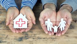 Hnde halten Papierfamilie und Papierhaus mit roten Kreuz