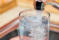 Closeup shot of a man pouring a glass of fresh water from a kitchen faucet