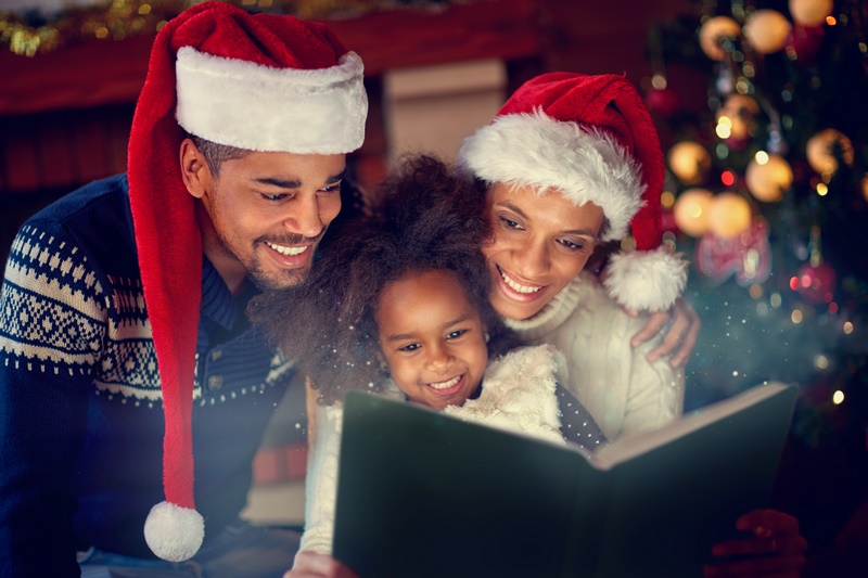 Young afro American parent together reading their little daughter Christmas fairytales